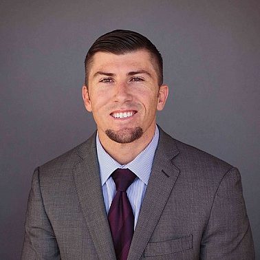 Portrait of a smiling Pastor with a neat haircut, wearing a gray suit, striped tie, and a white shirt against a gray background.