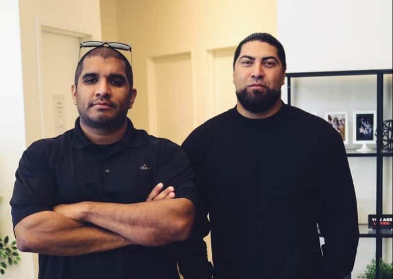 Two volunteer security guard standing with arms crossed in an office, one in a black polo and glasses, the other in a black sweater at Victory Baptist Church.