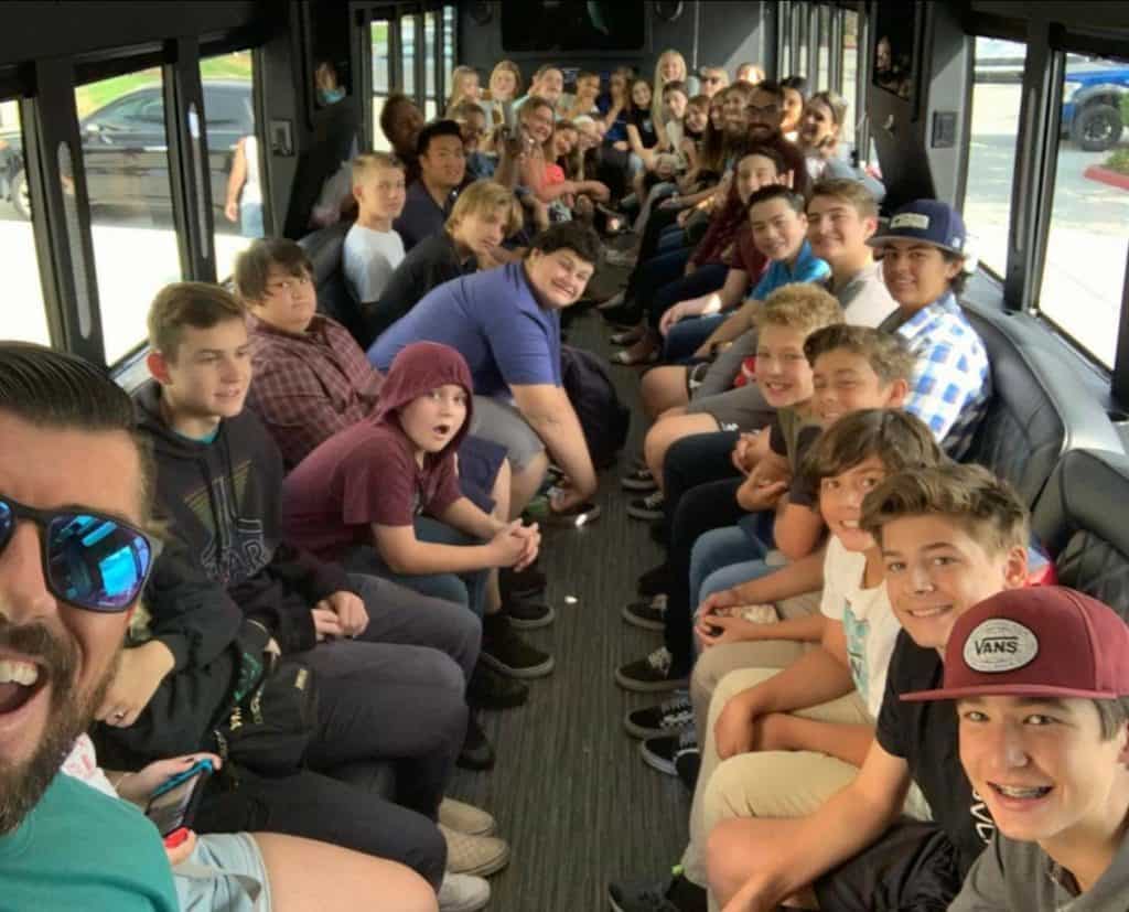 A group of diverse teenagers and an adult smiling and posing for a photo inside a crowded bus, part of the Youth Group.
