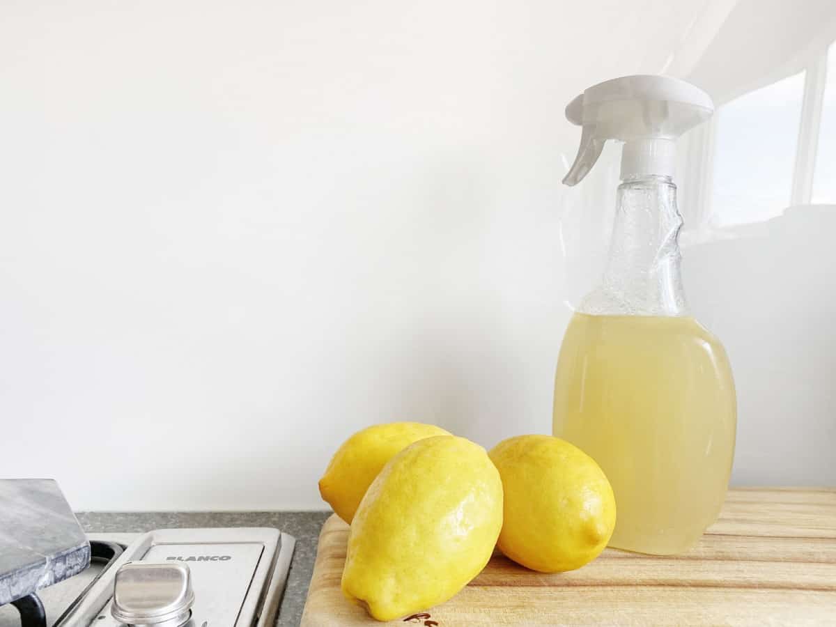 Three lemons on a wooden countertop next to a spray bottle filled with lemon juice, with a bright, clean background, ready to serve.