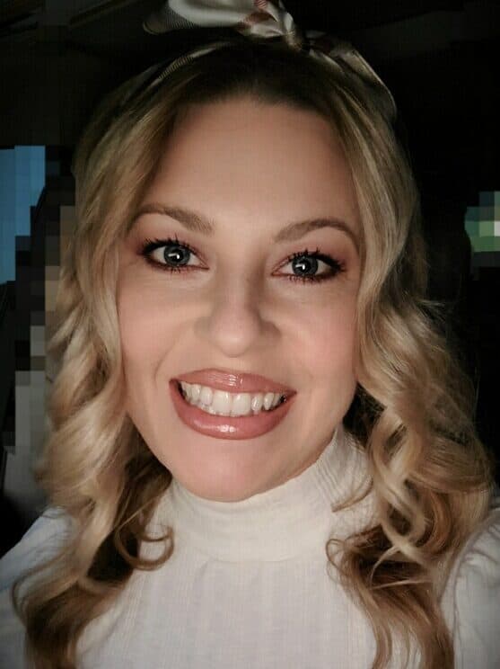 A person with curly blonde hair and a hairband, smiling warmly at the camera.