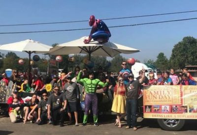 A group of volunteers dressed in various superhero costumes posing around and on a decorated trailer at the Lakeside Parade.